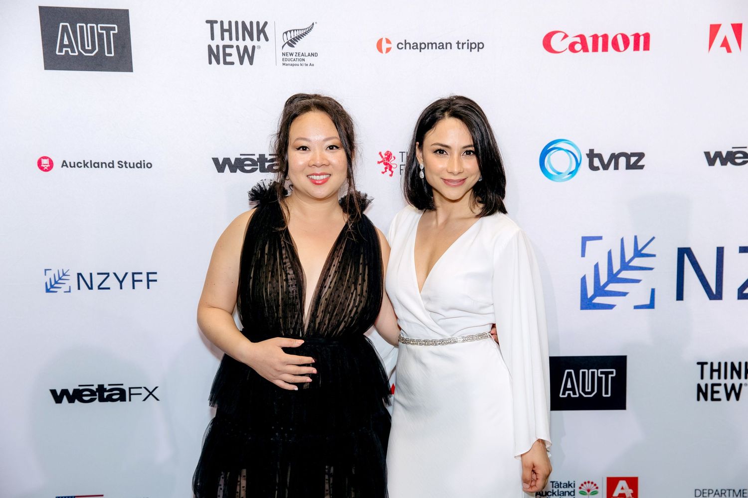 Two women posing for the camera in front of a media wall at a corporate event