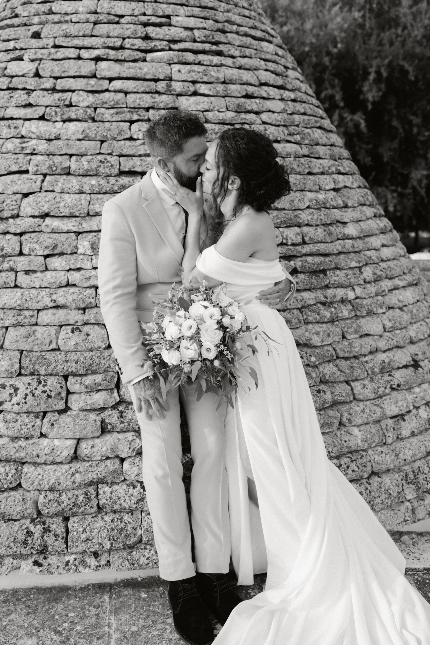 Black and white wedding photo series showing romantic moments between newlyweds against a stone wall backdrop.
