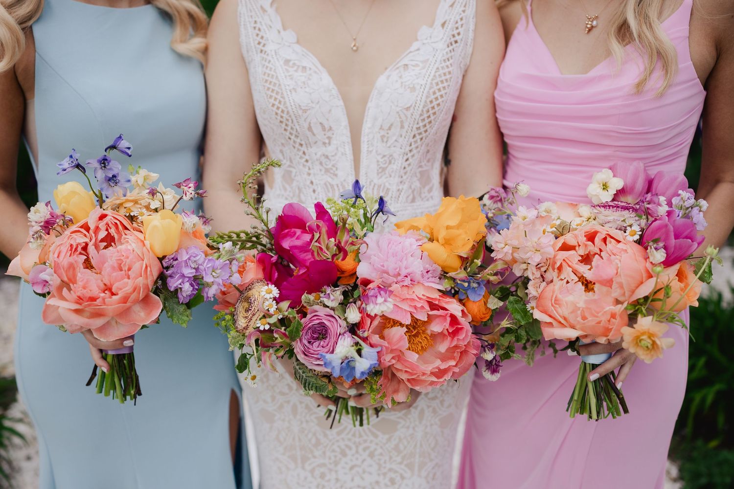 Close-up of bride and bridesmaids holding vibrant pink, orange, and purple floral wedding bouquets.