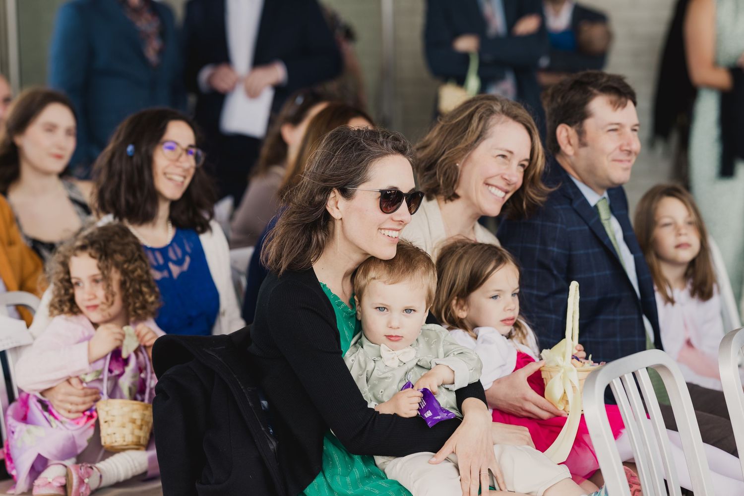 Wedding guests including children with Easter baskets sit and smile during an outdoor ceremony celebration.