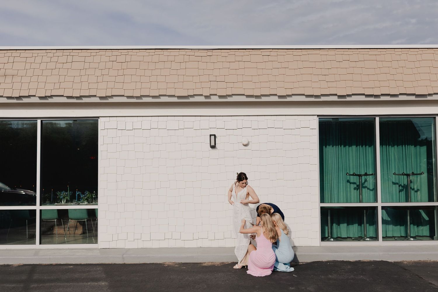 Three people pose casually outside a white brick building with large windows on a sunny day.