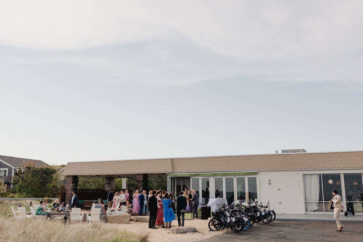 Wedding guests gather outside modern coastal venue building on a clear sunny day.