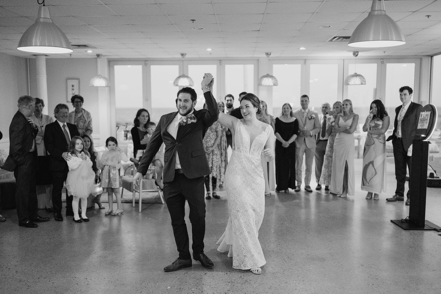 Bride and groom make a joyful entrance into their wedding reception as guests cheer and applaud around them.