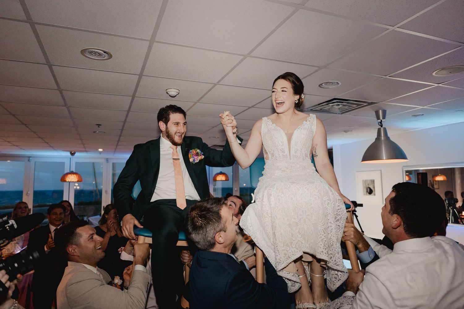 Bride and groom lifted by guests during a joyful hora dance at their wedding reception.