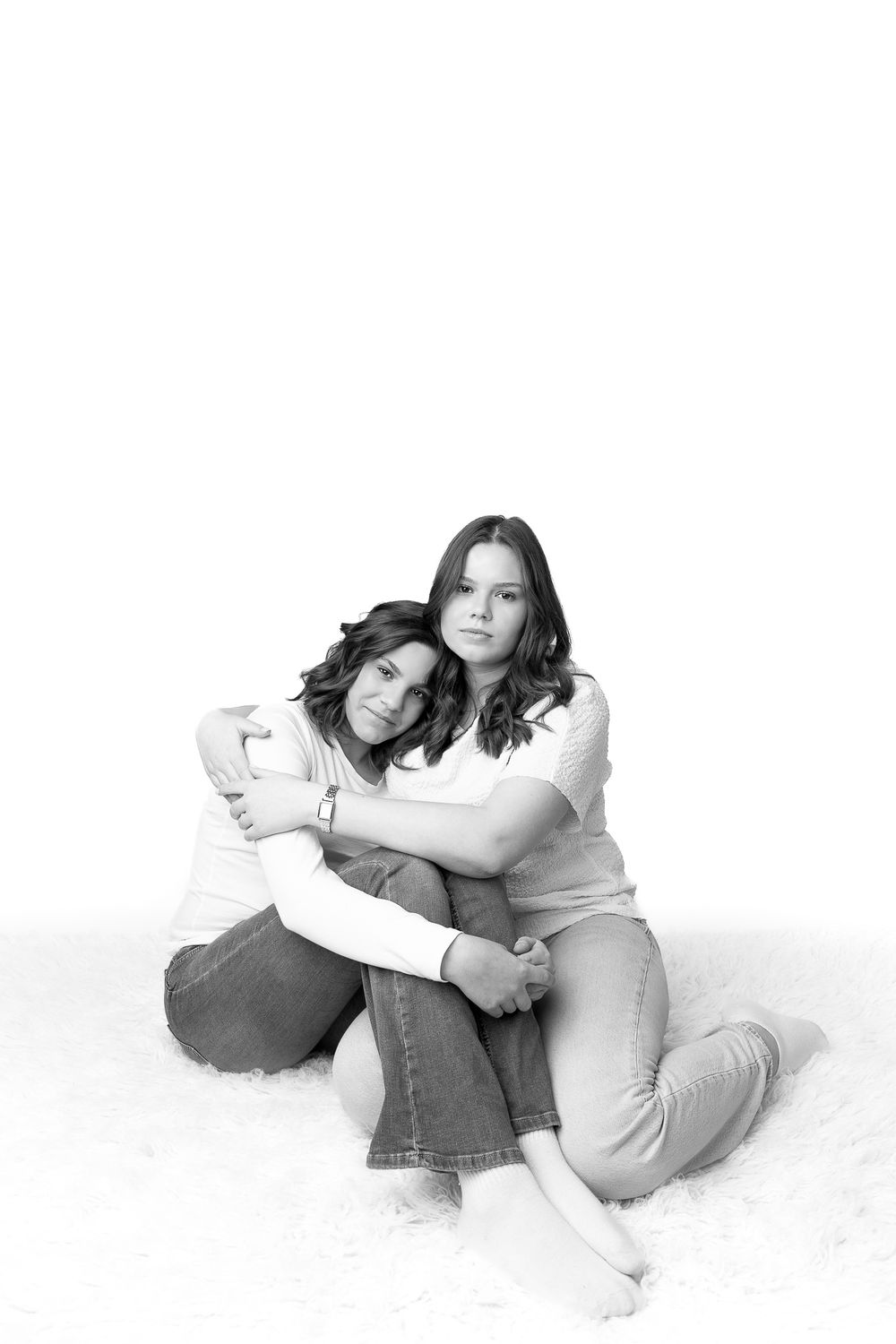 Black and white portrait of two women sitting on floor, embracing warmly in a close, affectionate pose.