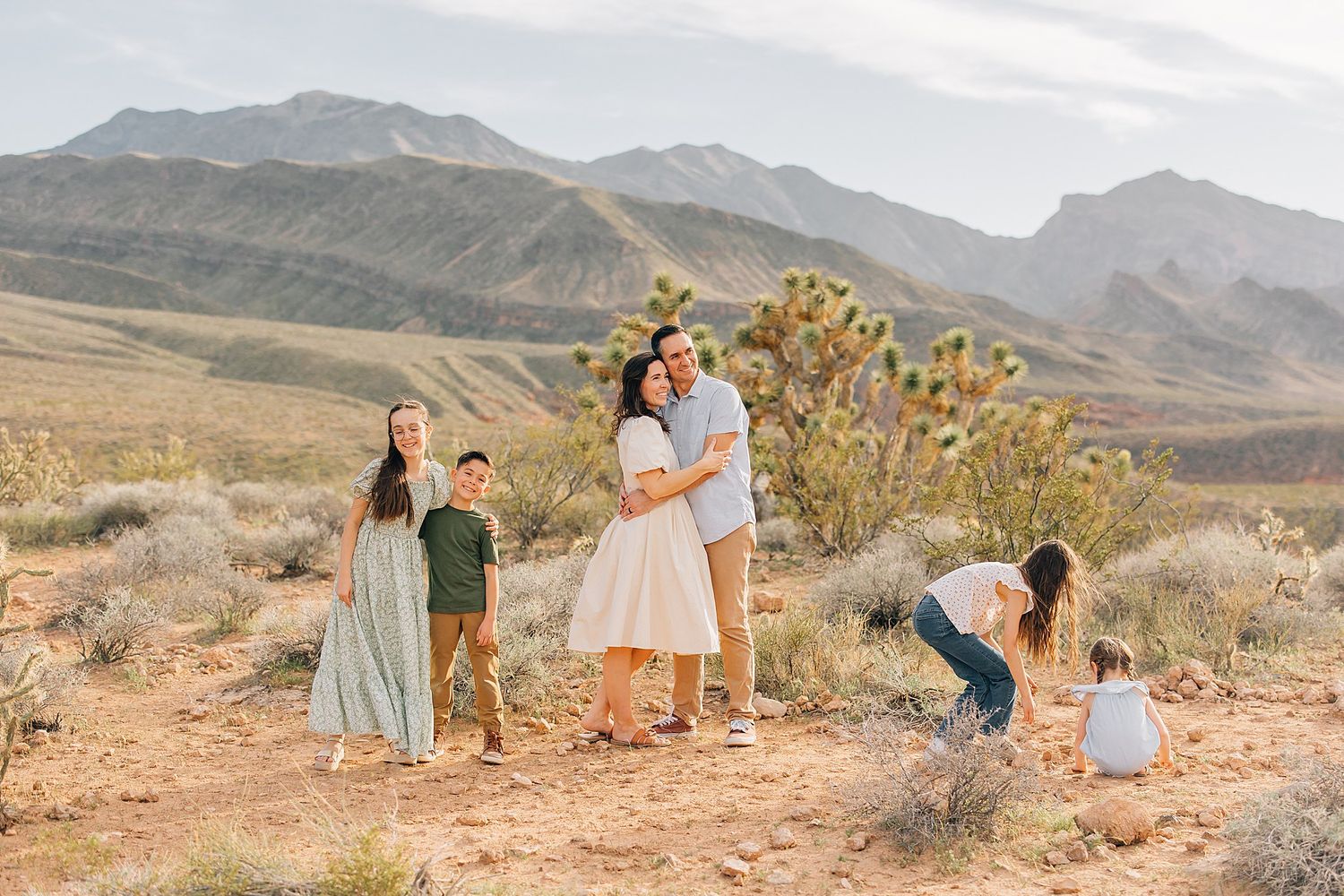 Family portrait in desert landscape with mountains, Joshua trees, and sandy terrain under soft natural light.