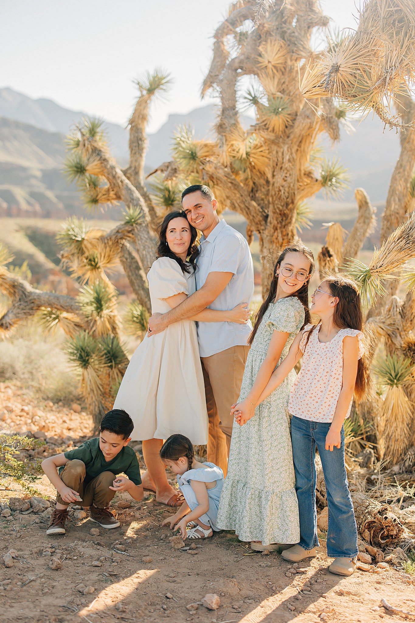 Family of six posing outdoors in desert landscape with Joshua trees and mountains in background.