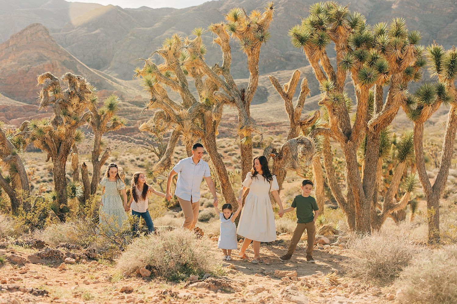 Family walking among Joshua trees in a sunny desert landscape with golden hills in the background.