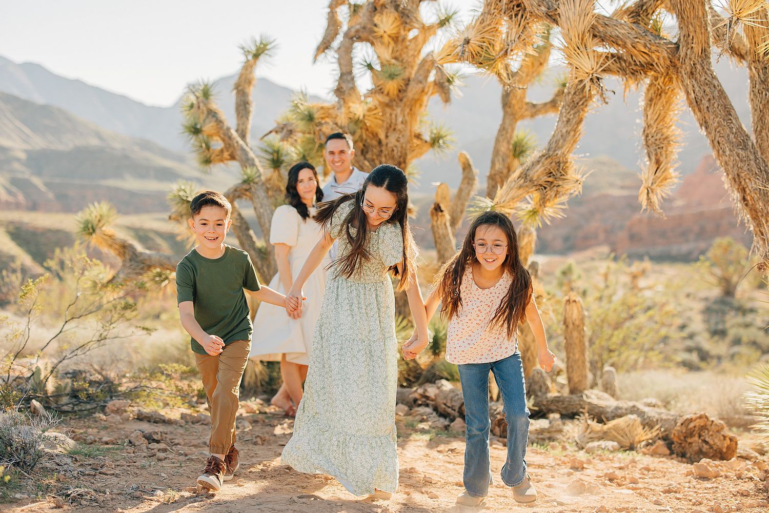 Family with two adults and three children playing outdoors near Joshua trees in a sunny desert landscape.