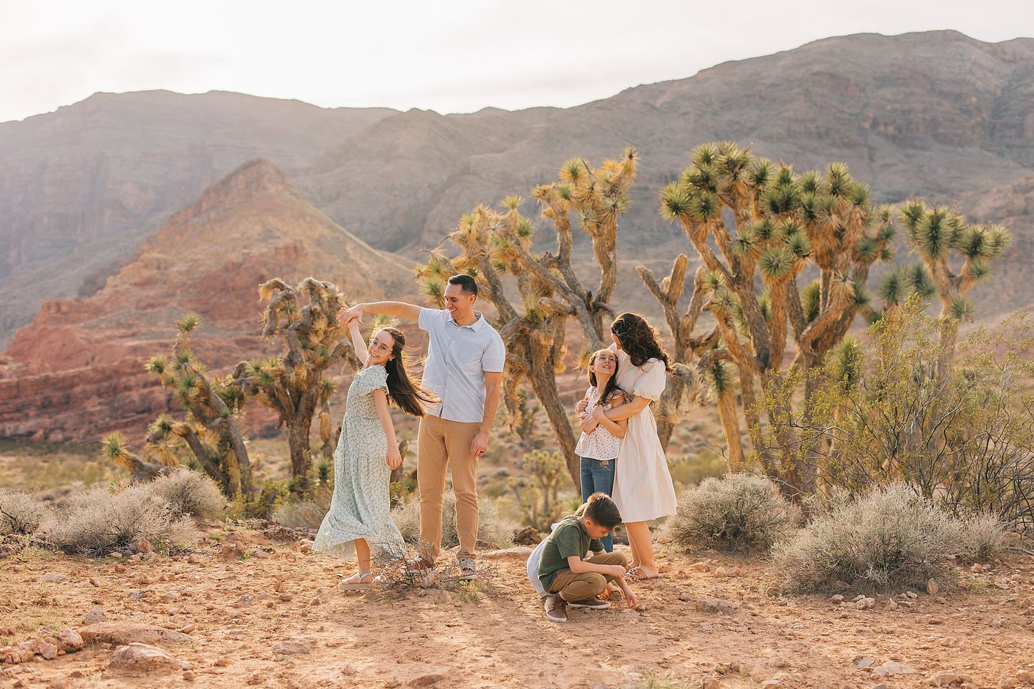 Family posing among Joshua trees in a desert landscape with red rock mountains in the background.