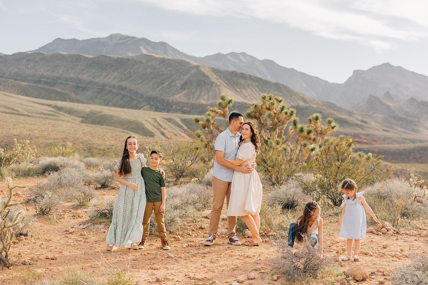 Family posing together in a scenic desert landscape with mountains and Joshua trees in the background.
