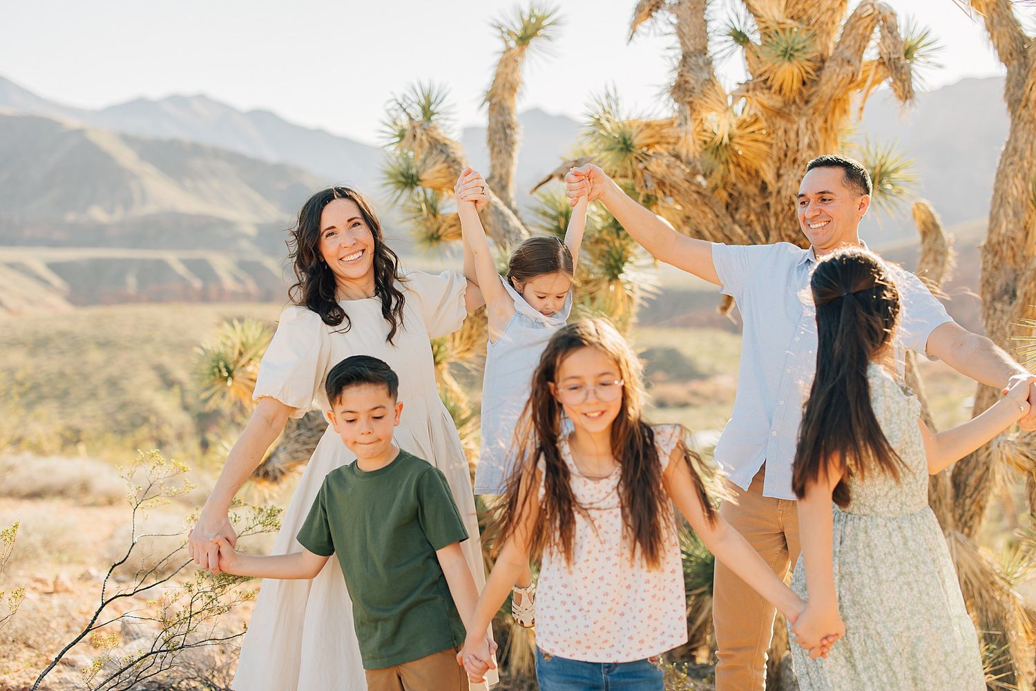 Happy family with children posing outdoors in desert landscape with Joshua trees and mountains in background.