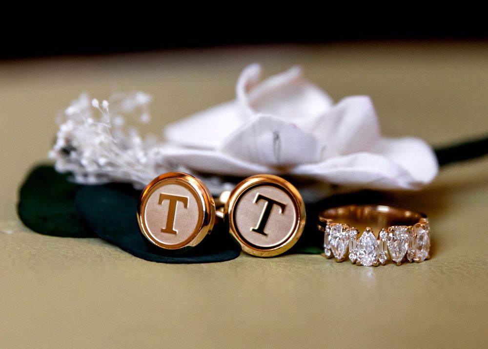 Gold monogram T cufflinks beside a sparkling diamond eternity band ring on an elegant wedding flat lay.