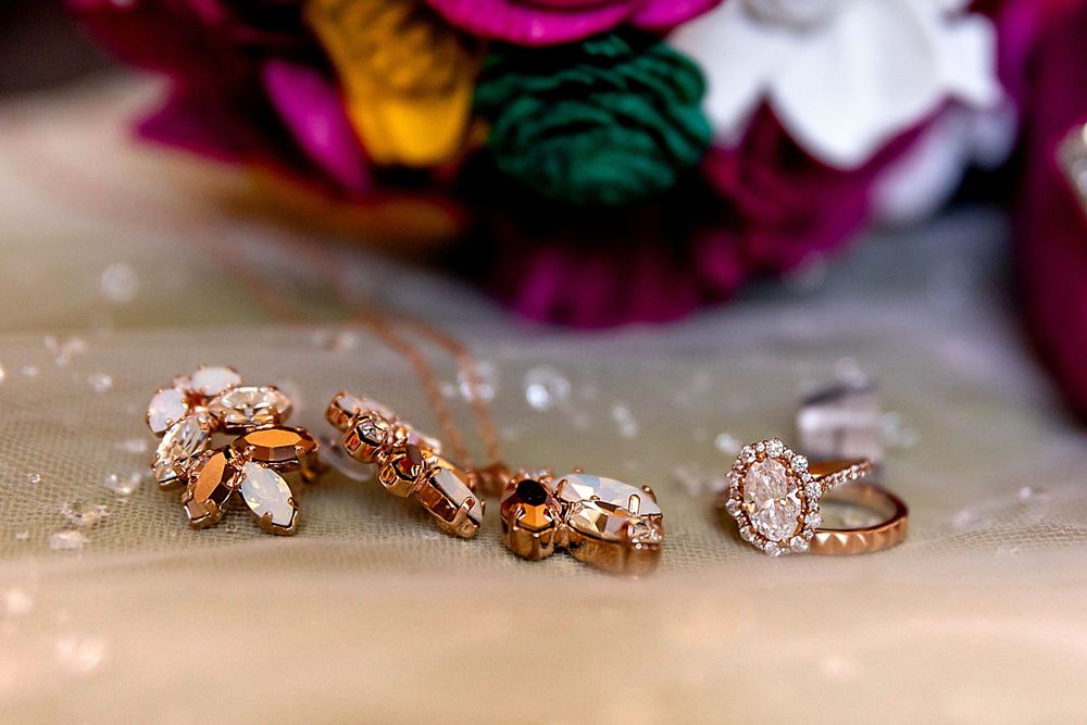 Rose gold bridal jewelry set featuring floral earrings, pendant necklace, and halo engagement ring displayed near colorful flowers.