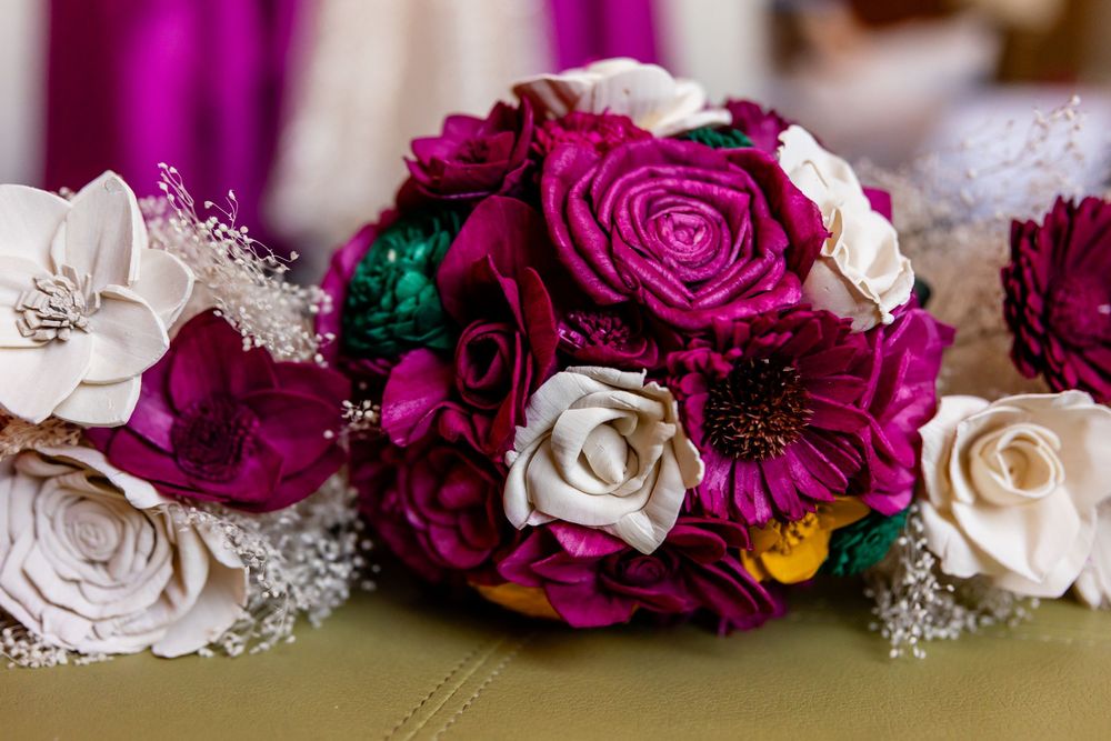 Elegant wedding bouquet featuring magenta roses, white flowers, and teal accents arranged on a gold tablecloth.