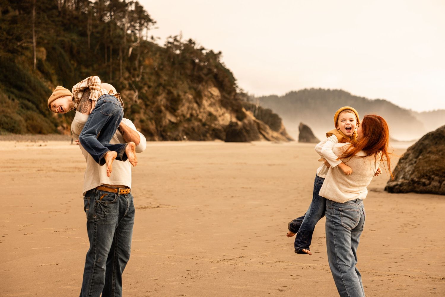 Pregnant couple holding hands in a field with rolling hills, wearing cream outfits during an outdoor maternity photoshoot.