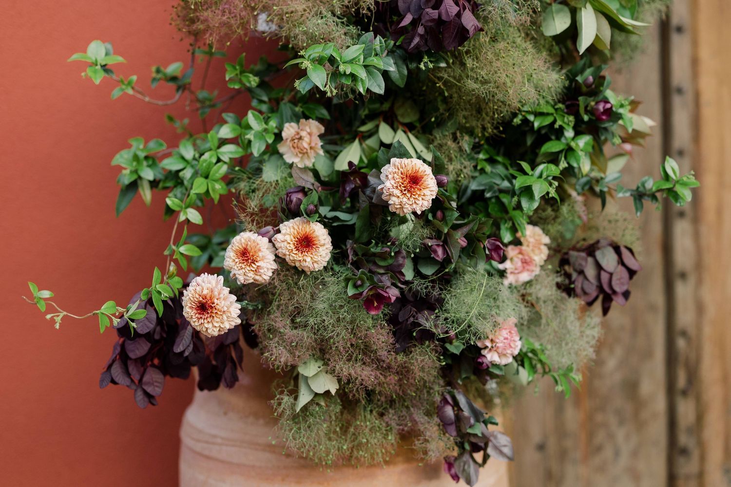 Lush floral arrangement with pink dahlias and dark purple blooms against a terracotta wall.