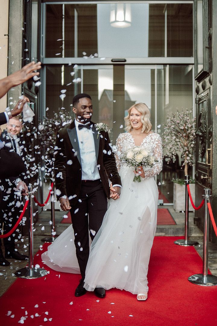 Newlyweds celebrate on red carpet as confetti rains down during their wedding exit celebration.