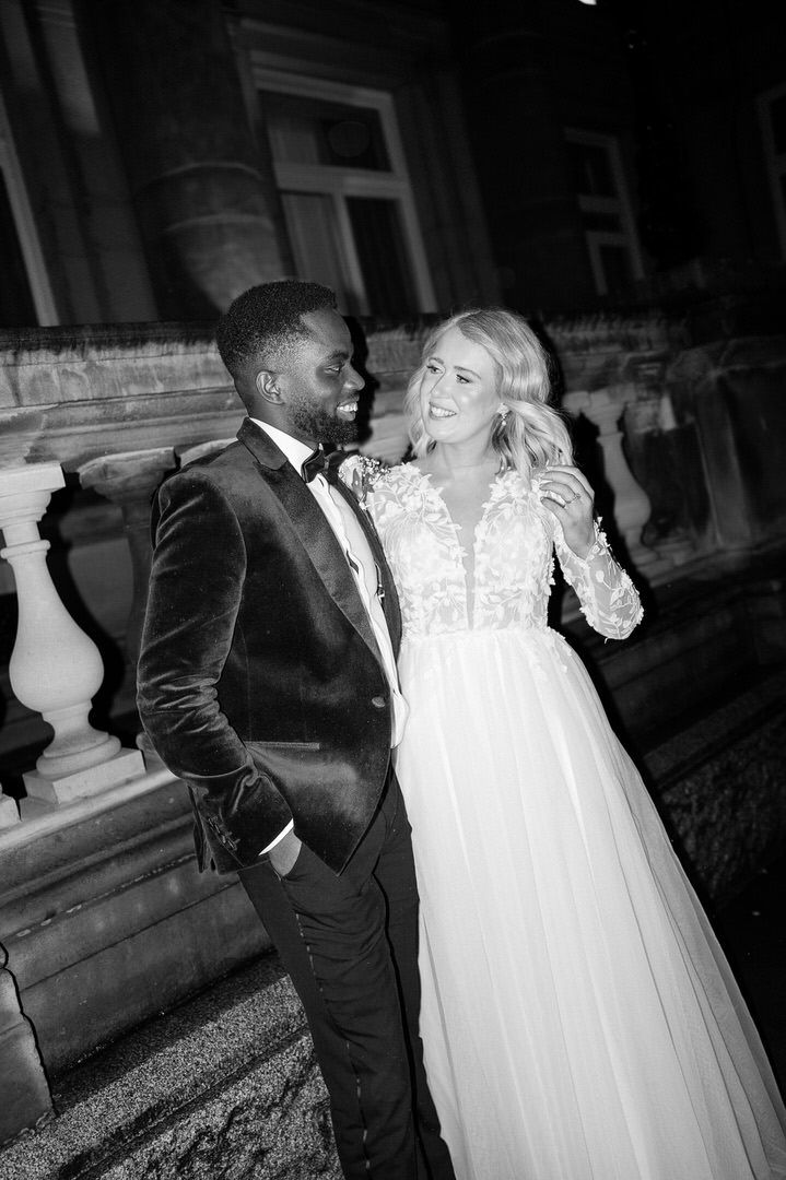 A happy couple shares a joyful moment on their wedding day, with the bride in white and groom in black velvet tuxedo.