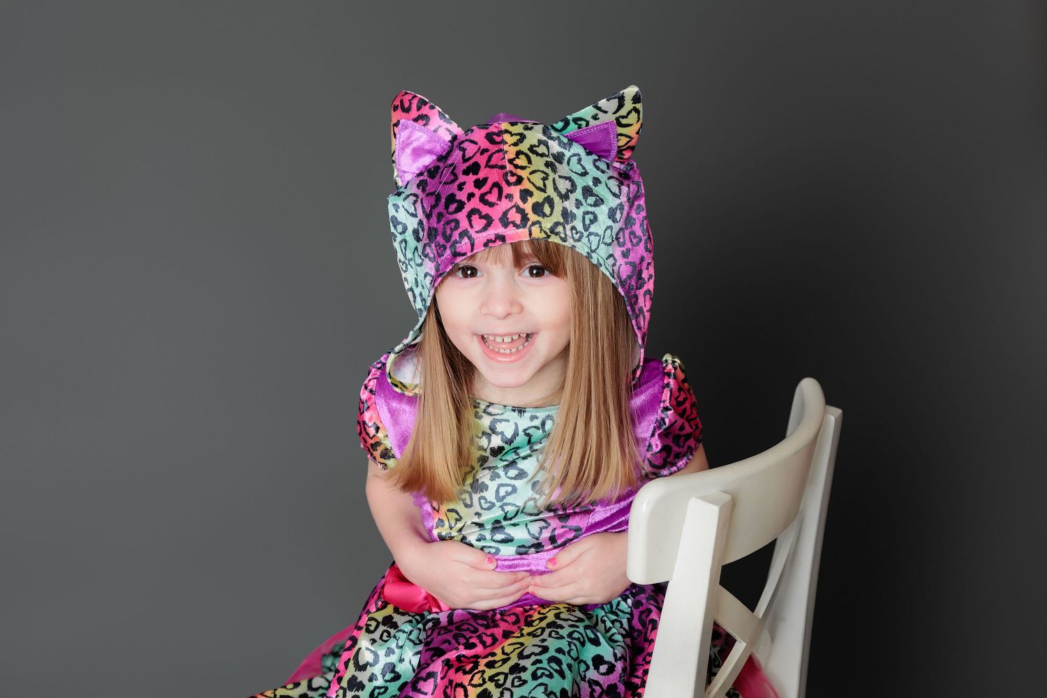 A person wearing a colorful floral print hoodie poses in a chair against a dark background.