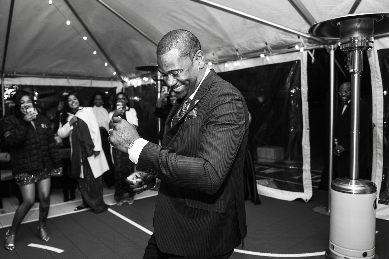 A person in a dark suit checks their watch while dancing under an outdoor tent at an event.