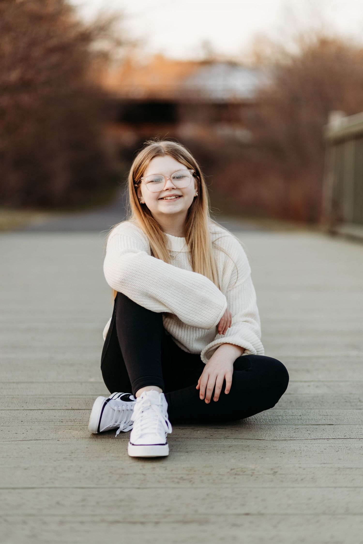 A person in black pants and white sneakers sits casually on a concrete surface during autumn.