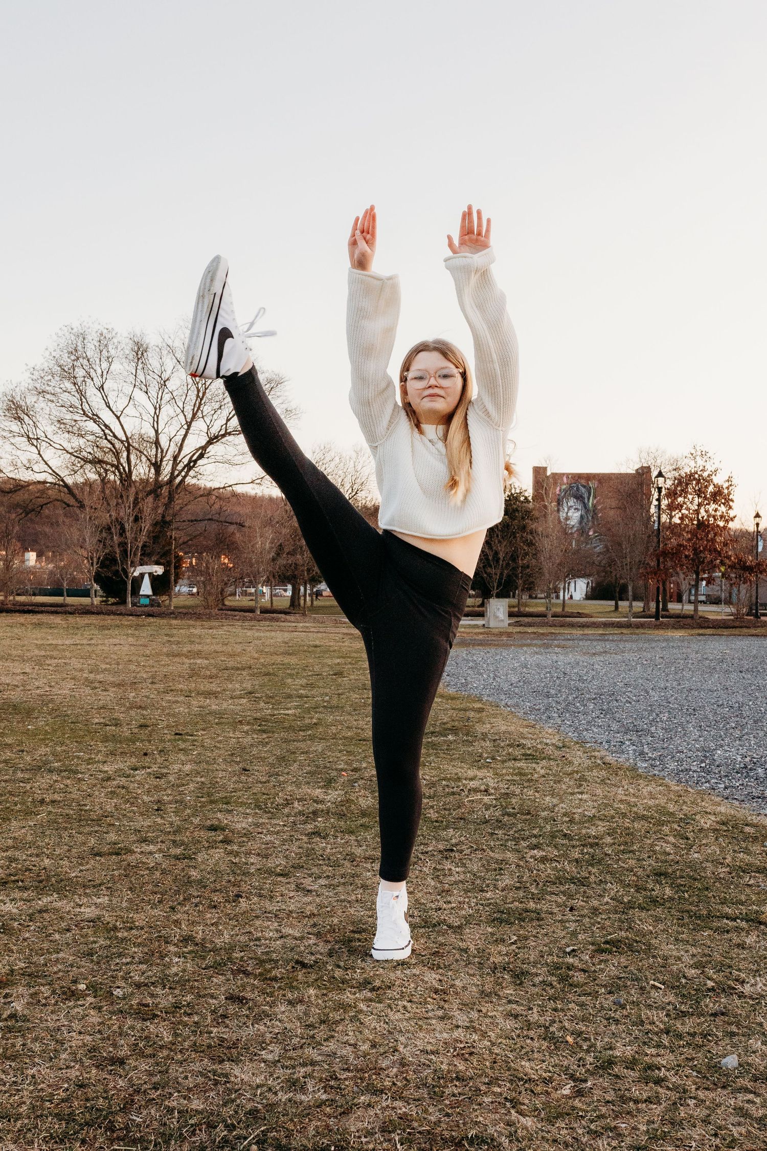 Person in black pants performs high leg kicks in a grassy field at sunset.