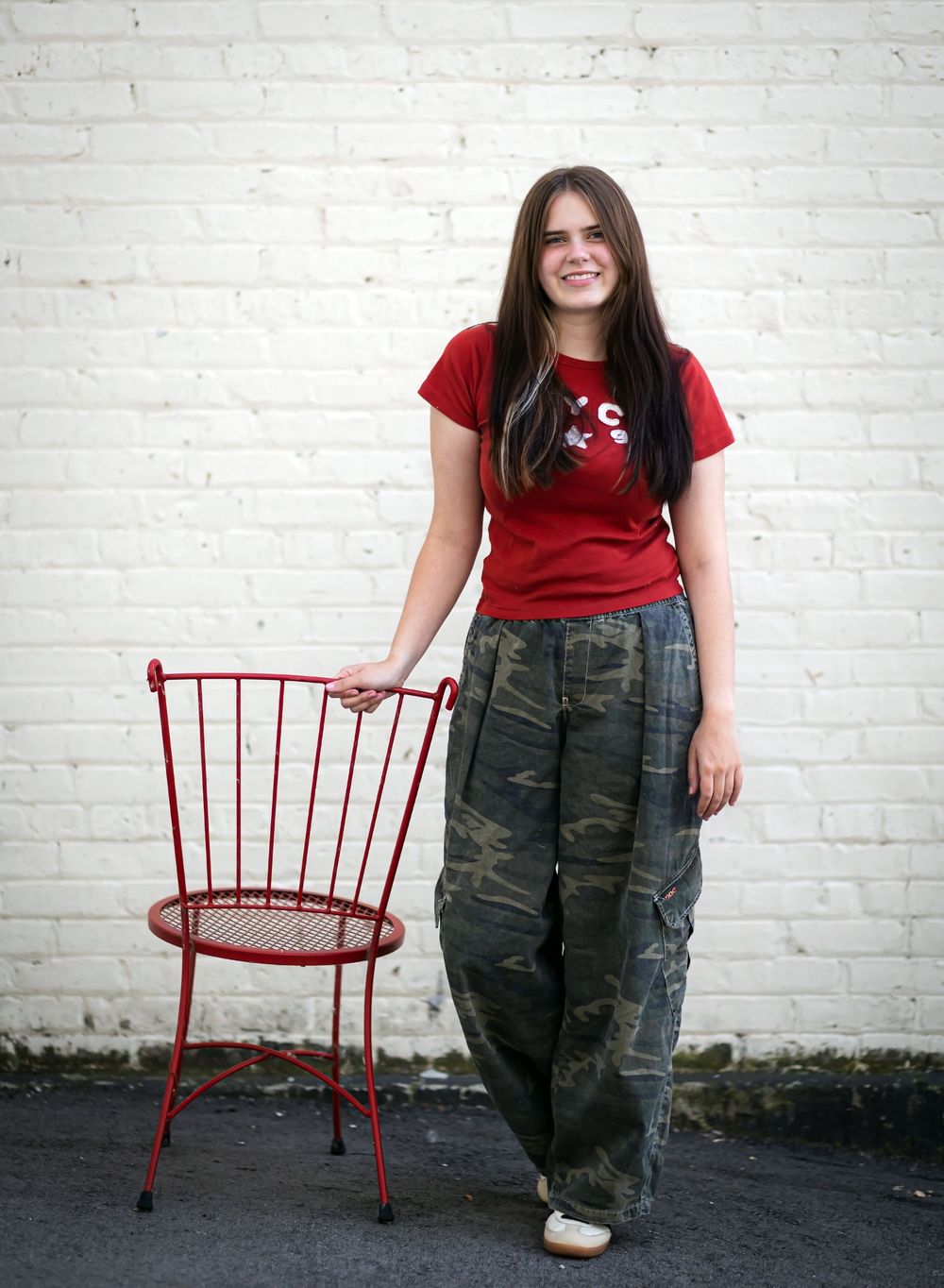 A series of four photos showing someone in a red shirt and camo pants posing with a red vintage-style chair against a white wall.