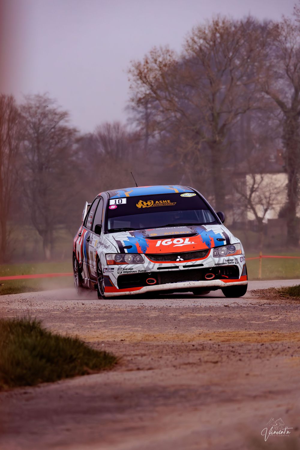 Rally car navigates a dirt track turn in sequence, kicking up dust as it speeds through the challenging terrain.