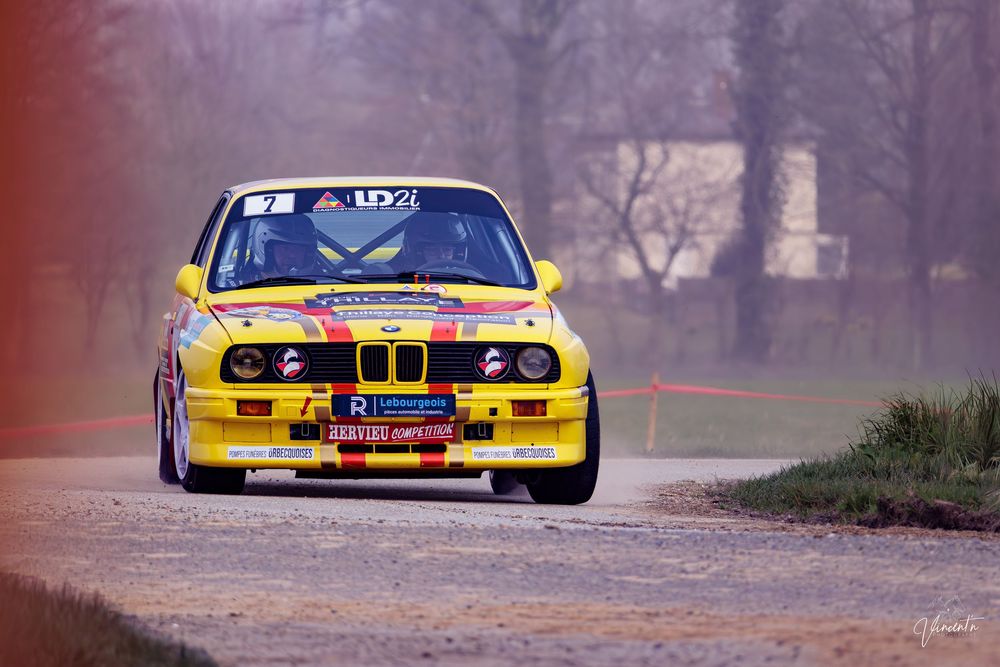 Yellow and blue race cars compete on a foggy track during a motorsport competition.