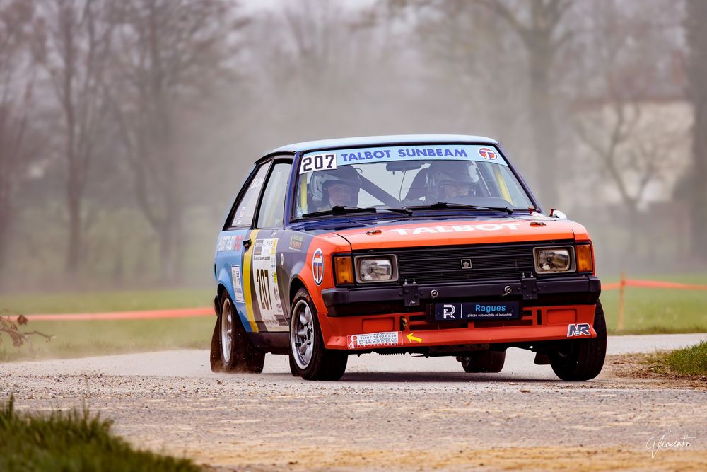 Racing cars speeding along a track during a competitive motorsport event on a foggy day.