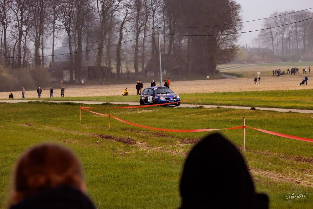 Rally car racing on a dirt track through foggy terrain as spectators watch from the sidelines.