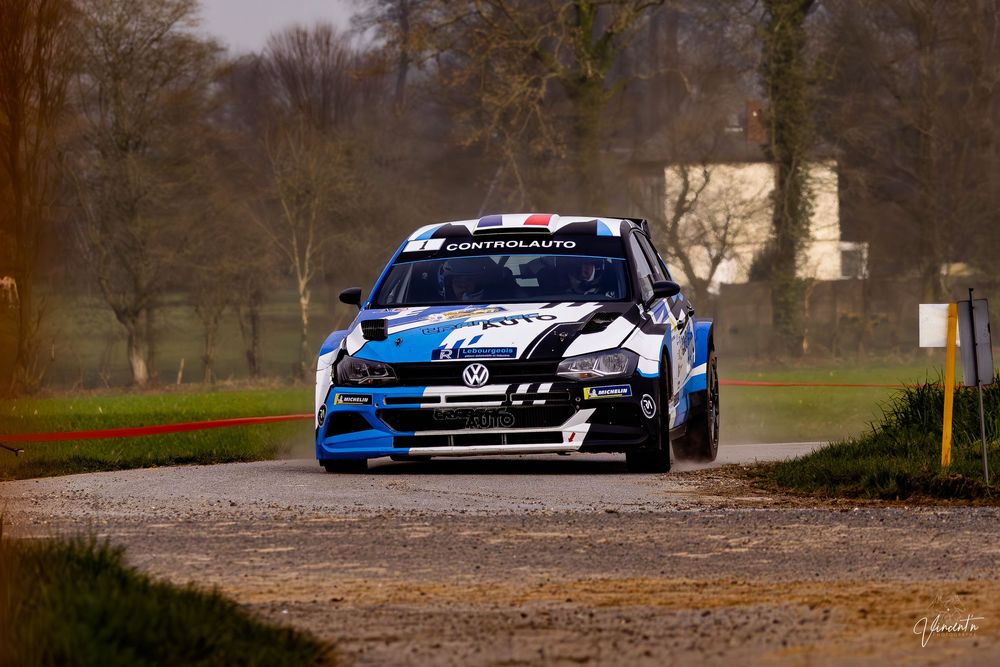 A blue and black race car speeds through a dirt track during a rally competition.