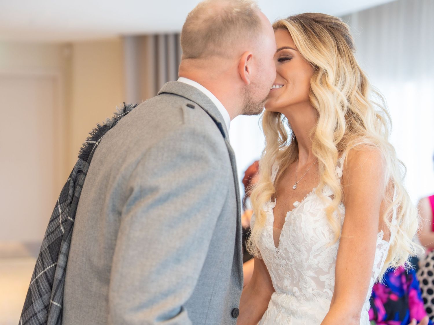 Romantic wedding couple sharing an intimate kiss in a sunlit venue.