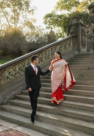 A couple in formal attire descends a grand stone staircase in a park during autumn.