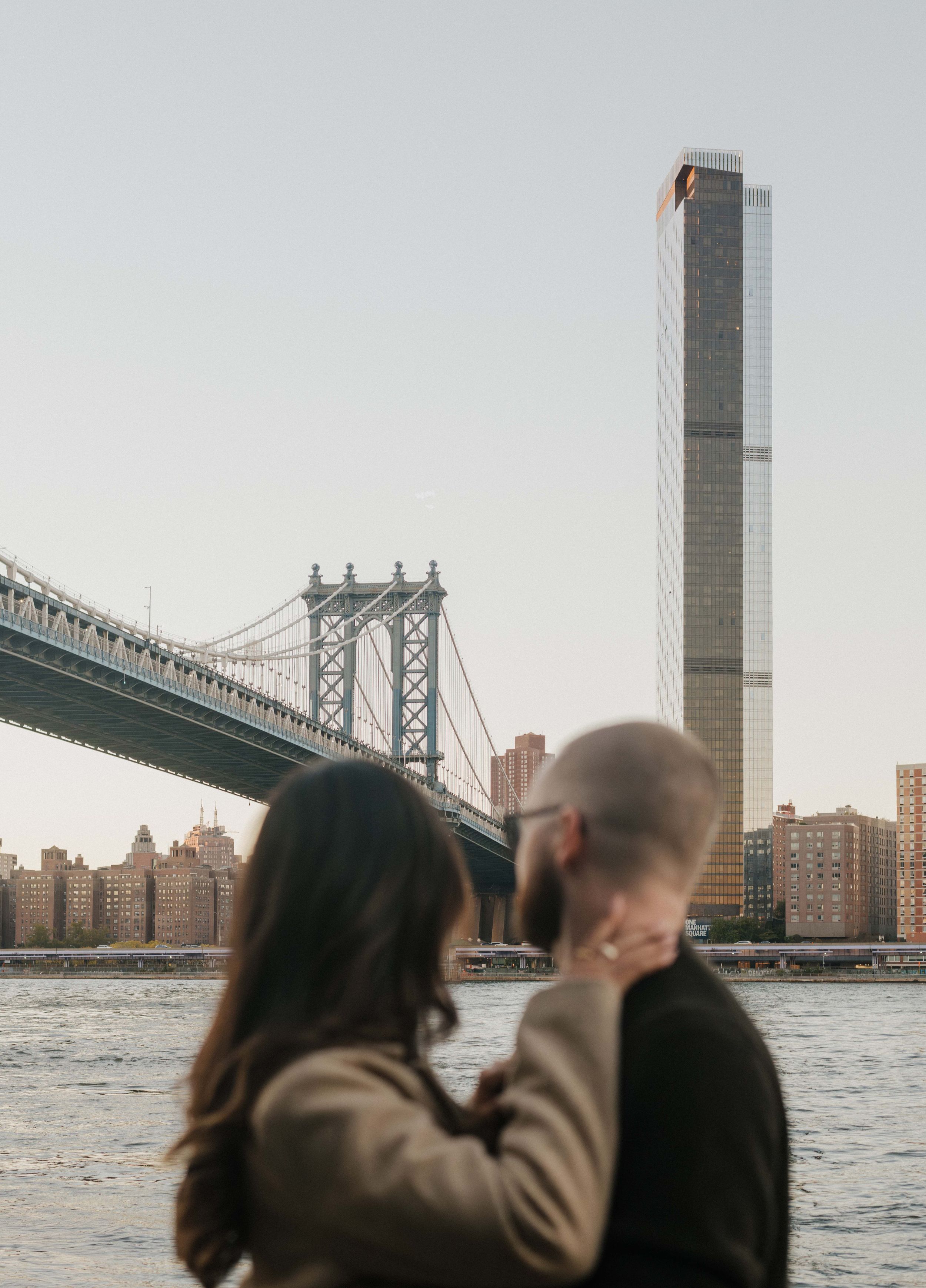 Silhouettes of people looking at Manhattan Bridge and skyline across East River during sunset in New York City.