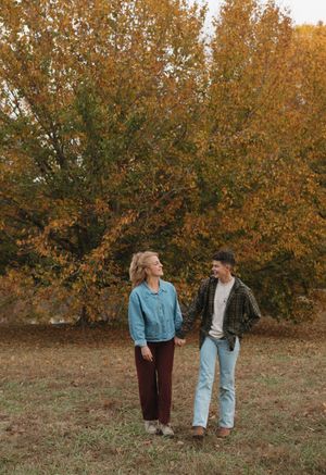 A couple walks together through a scenic autumn landscape with golden foliage in the background.