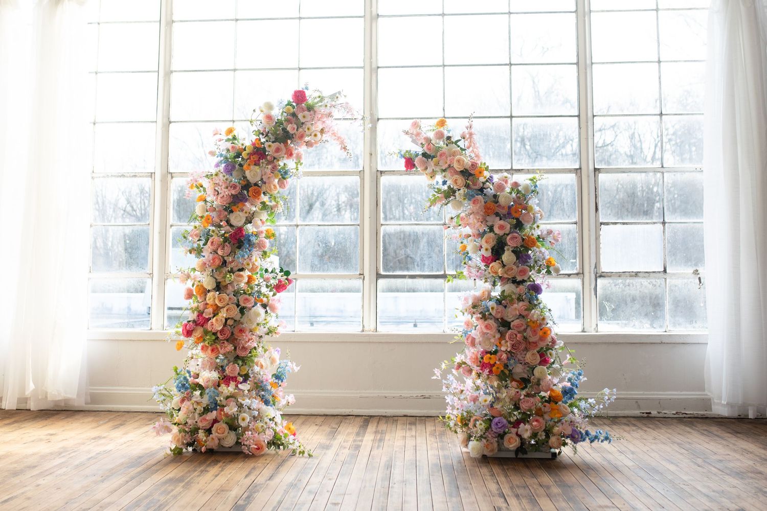 A bright, airy white studio space with a floral arch decorated in pink and peach blooms near large windows.