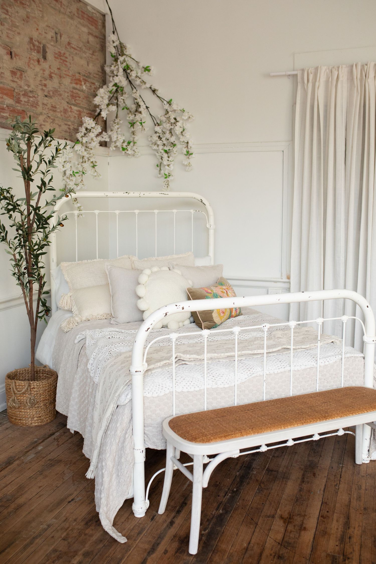 White iron bed frame with floral bedding and potted greenery against exposed brick wall in rustic farmhouse bedroom.