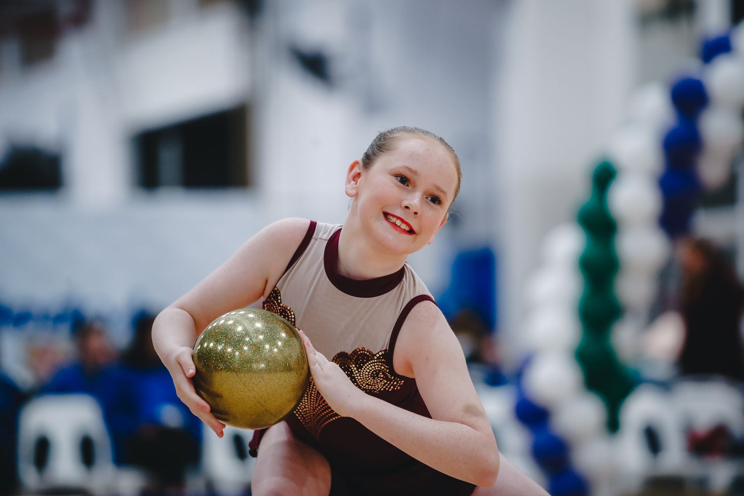 Young athlete practices with golden rhythmic gymnastics ball in training gym.