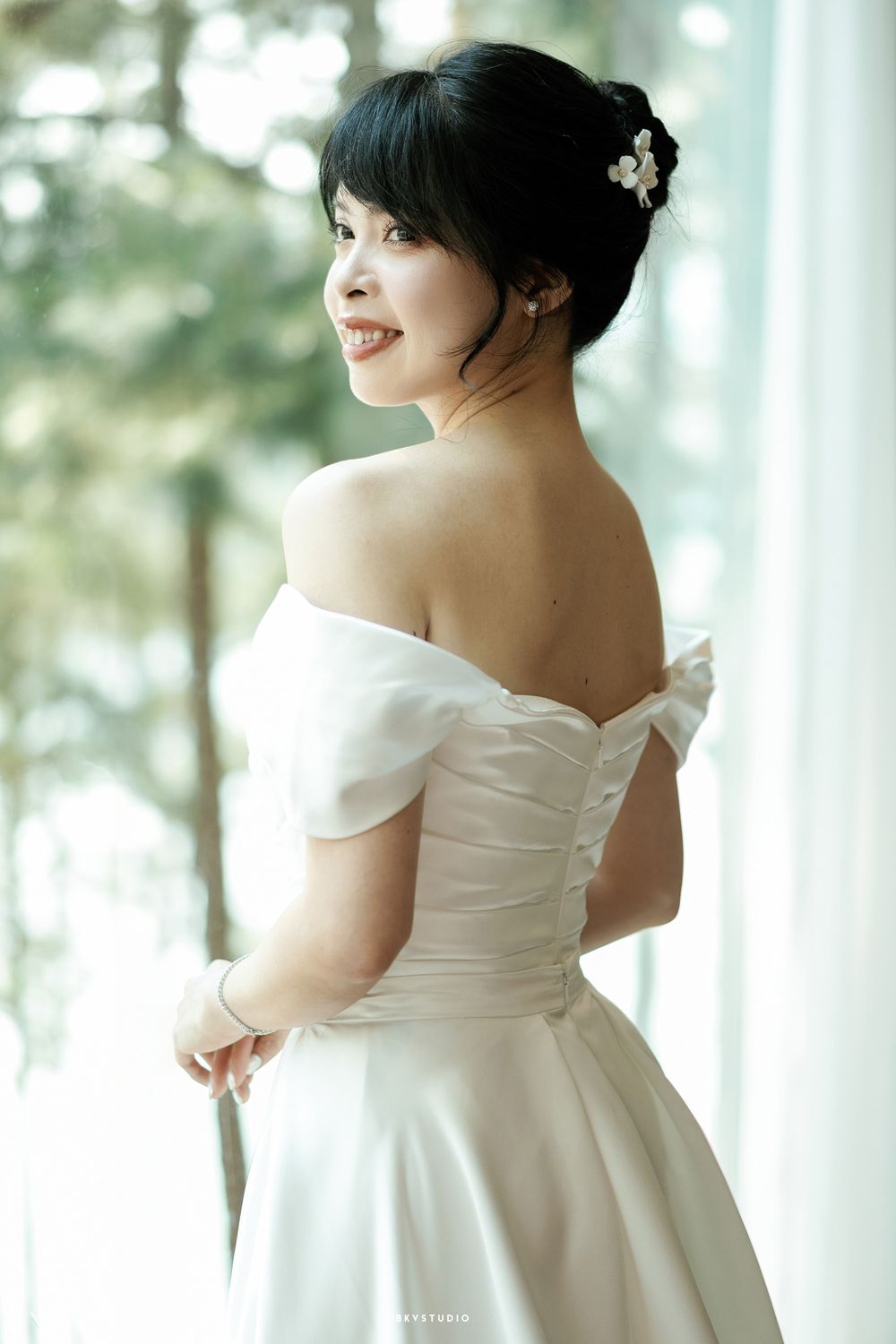 Elegant bridal portrait in off-shoulder wedding gown by window.