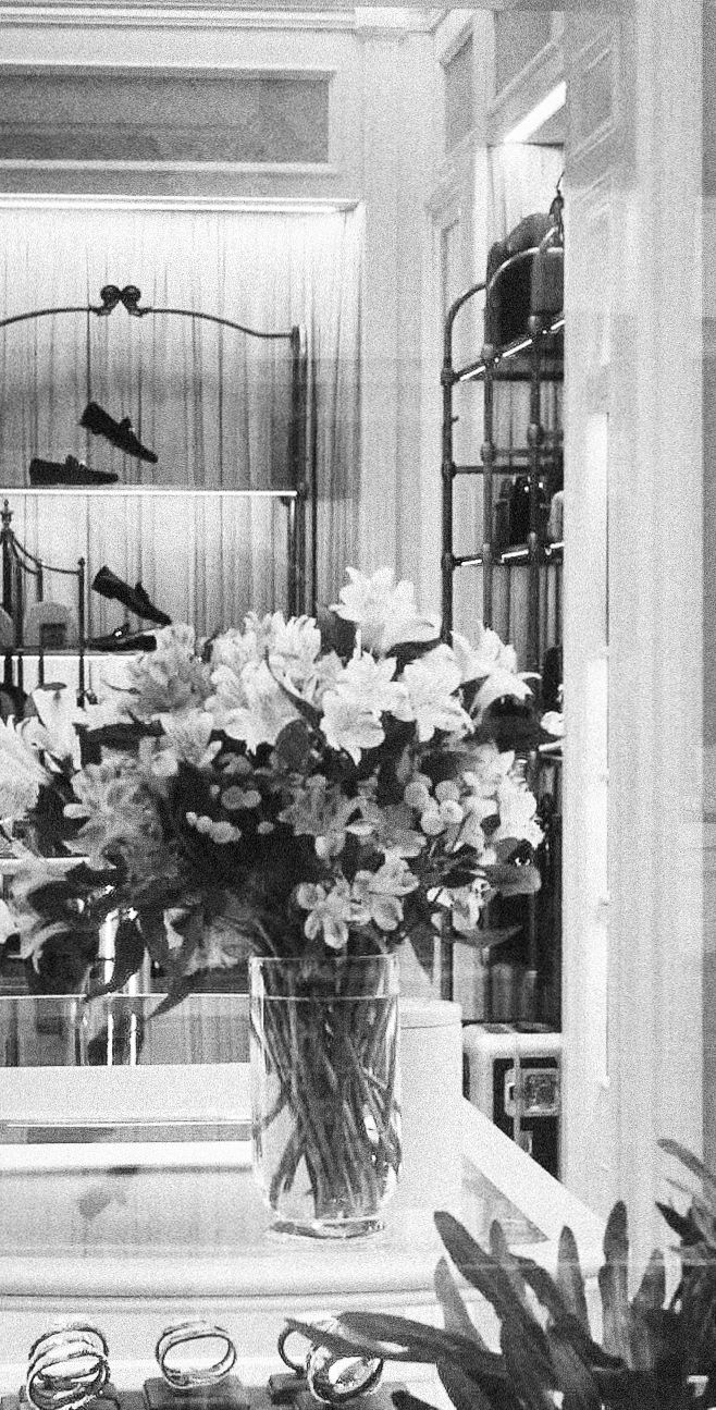 Black and white image of flower arrangements in vases displayed near windows with hanging lamps.