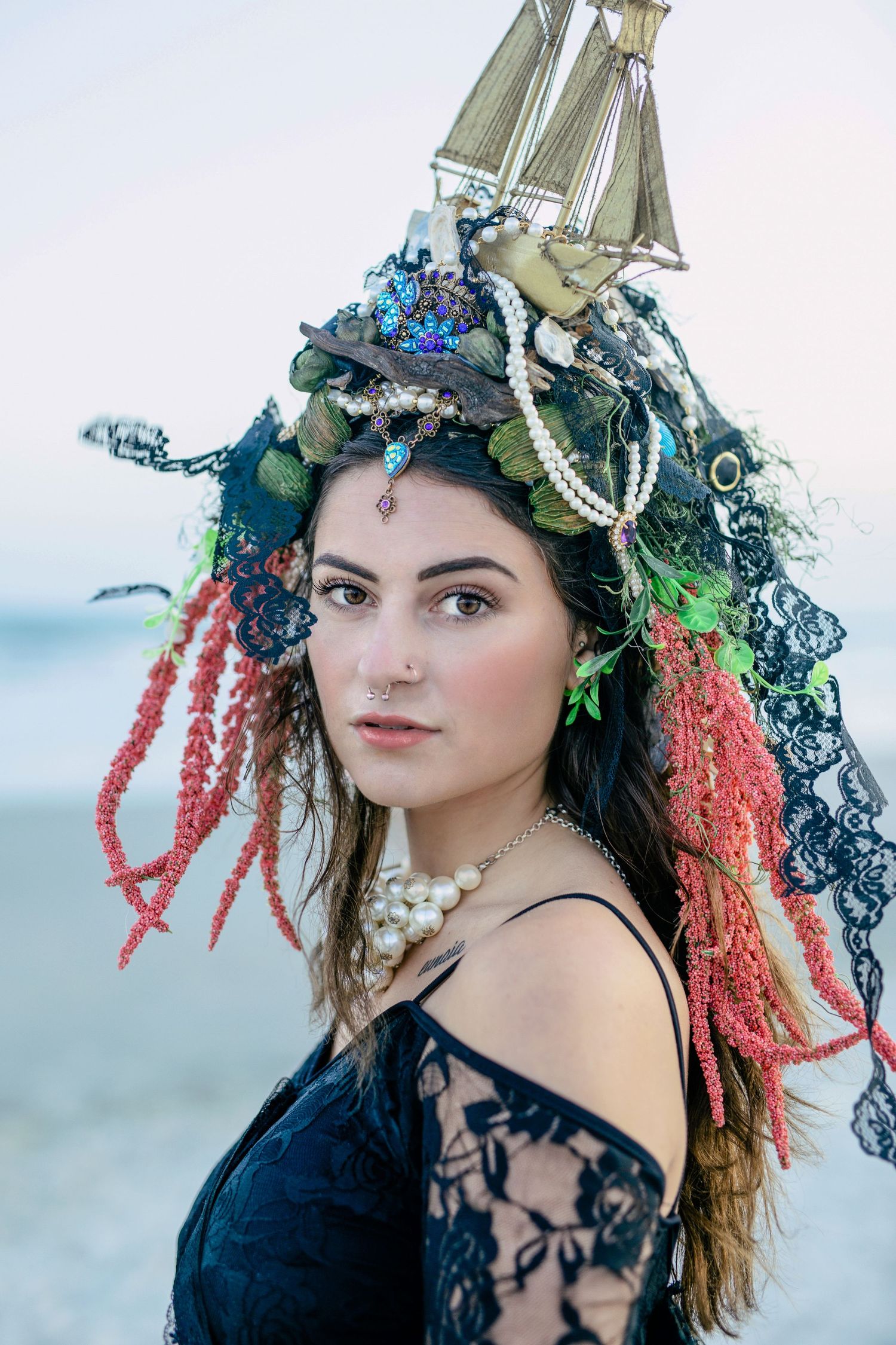 Woman in black dress at sunset, handmade ship headpiece, moody ocean-themed fantasy photo on a Windsor beach.