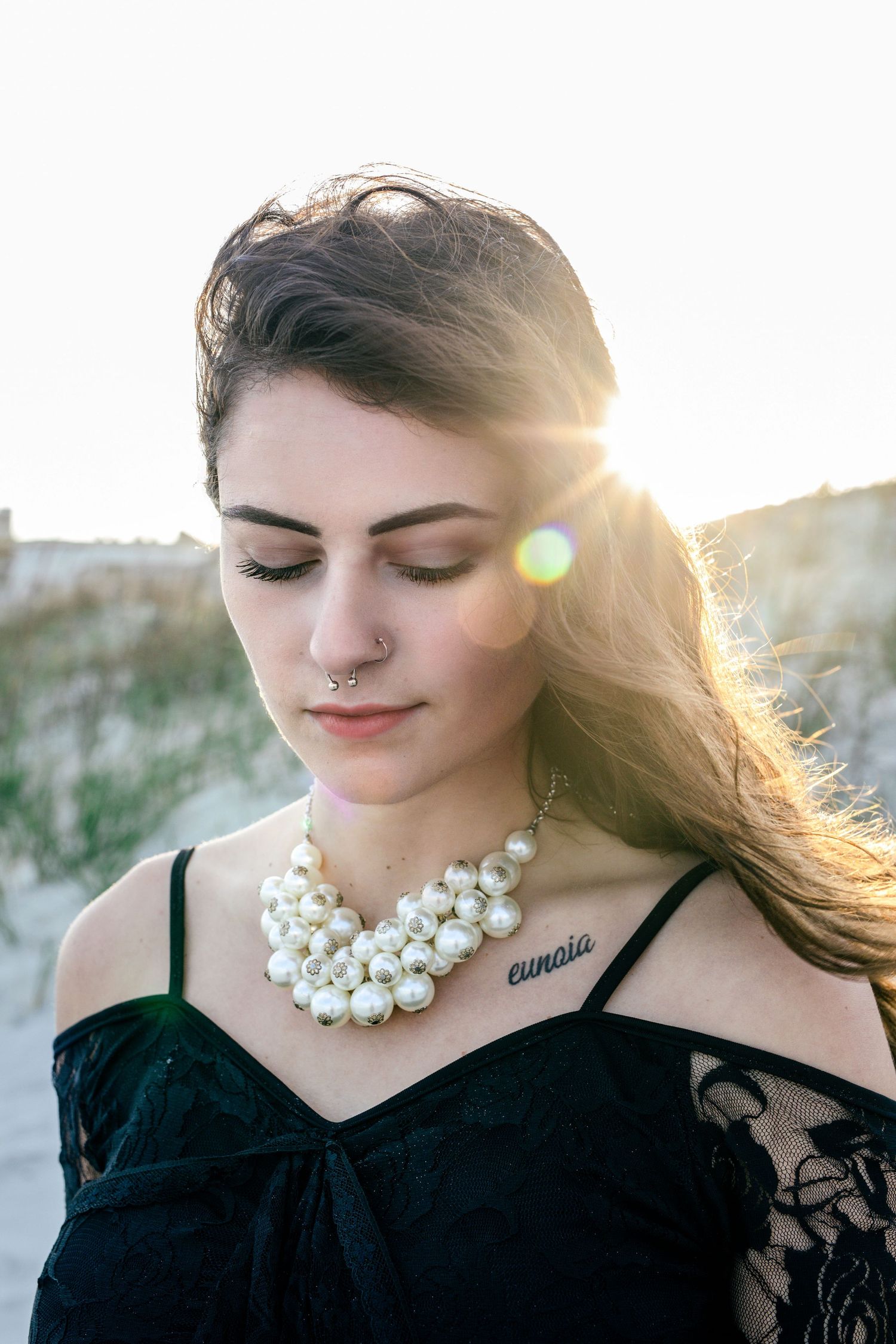 Windswept woman at beach in dramatic black dress, captured during golden hour – portrait photographer Essex County.