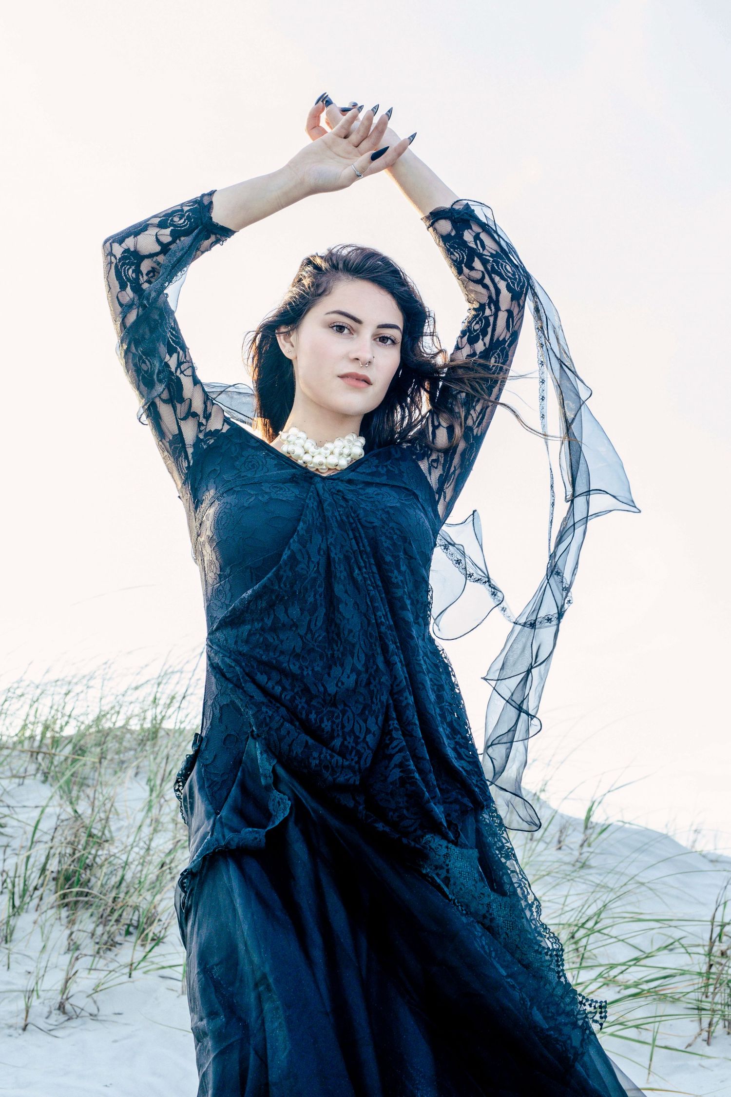 Graceful woman in black dress posing on shoreline at sunset, golden tones and soft elegance – Windsor portraiture.