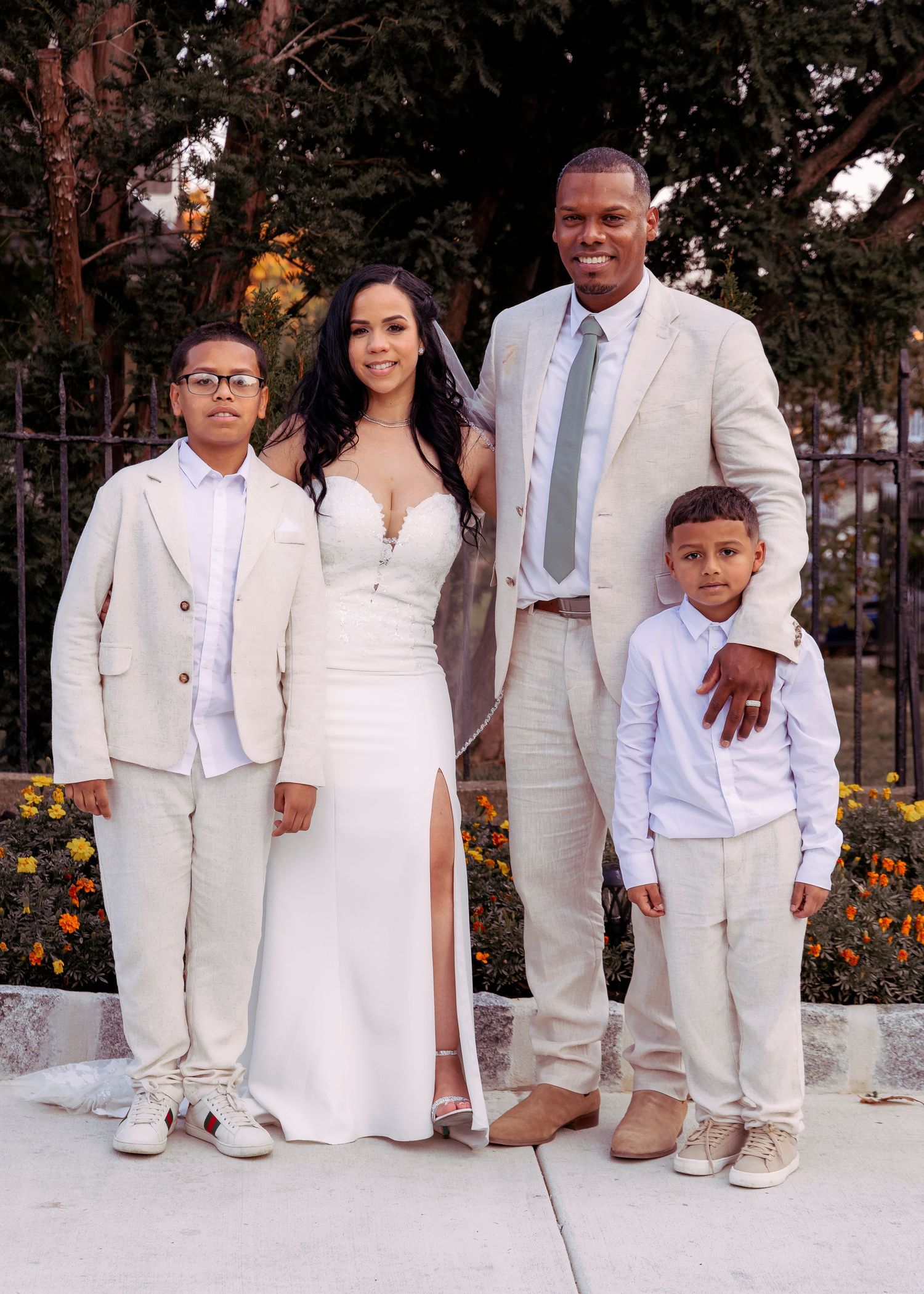 Family wedding portrait in coordinated white and cream formal attire with garden backdrop.
