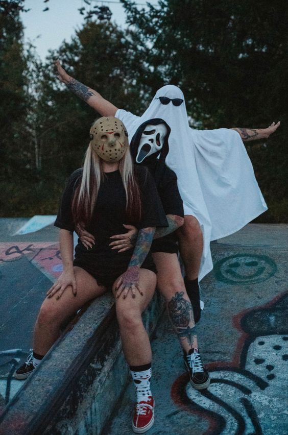 Two people in Halloween costumes pose at skate park, one wearing ghost mask and one in dark outfit.