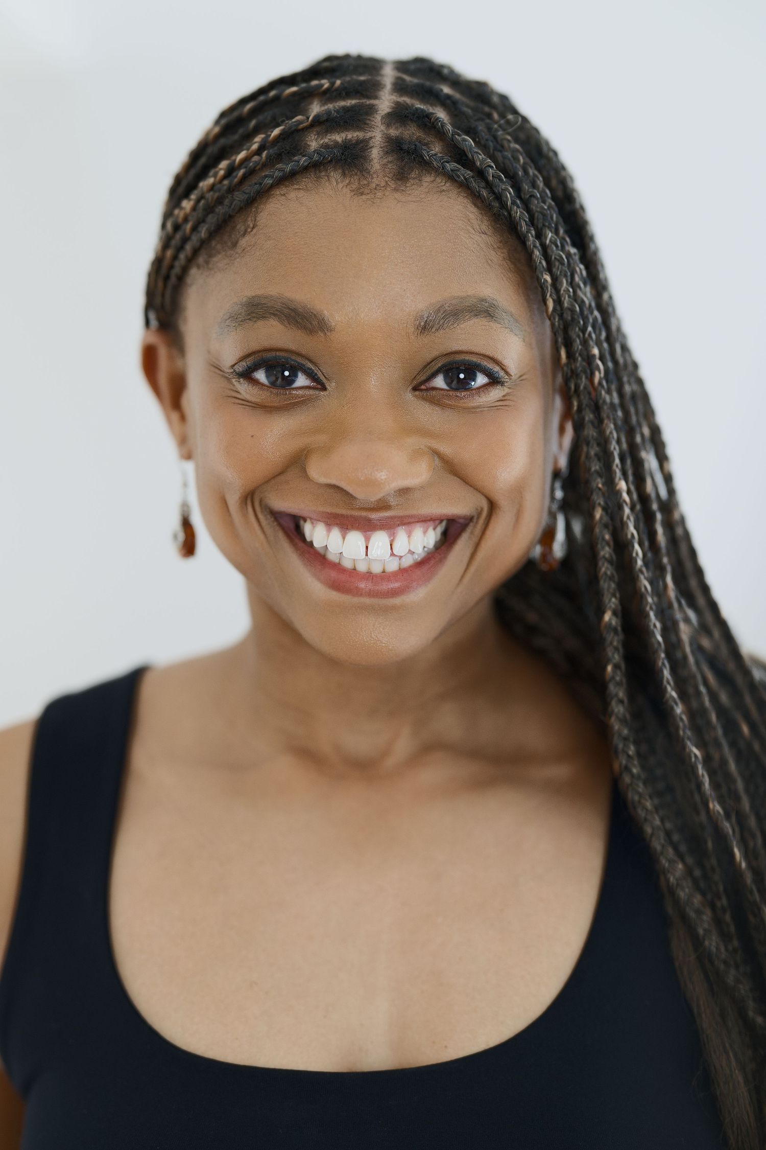 Studio portrait with braided hairstyle and black tank top against white background.