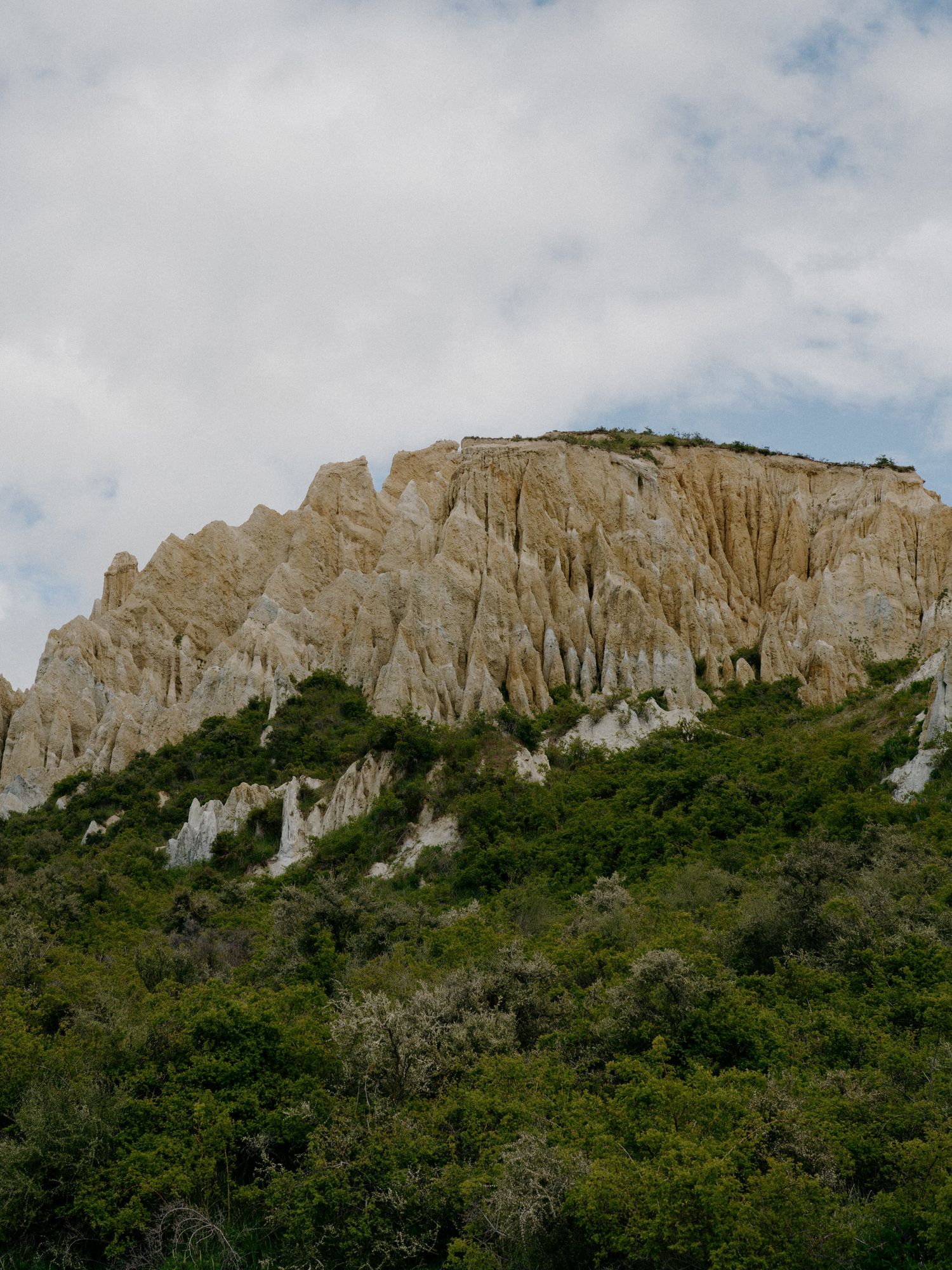 Towering limestone cliffs rise above green vegetation against a cloudy sky.