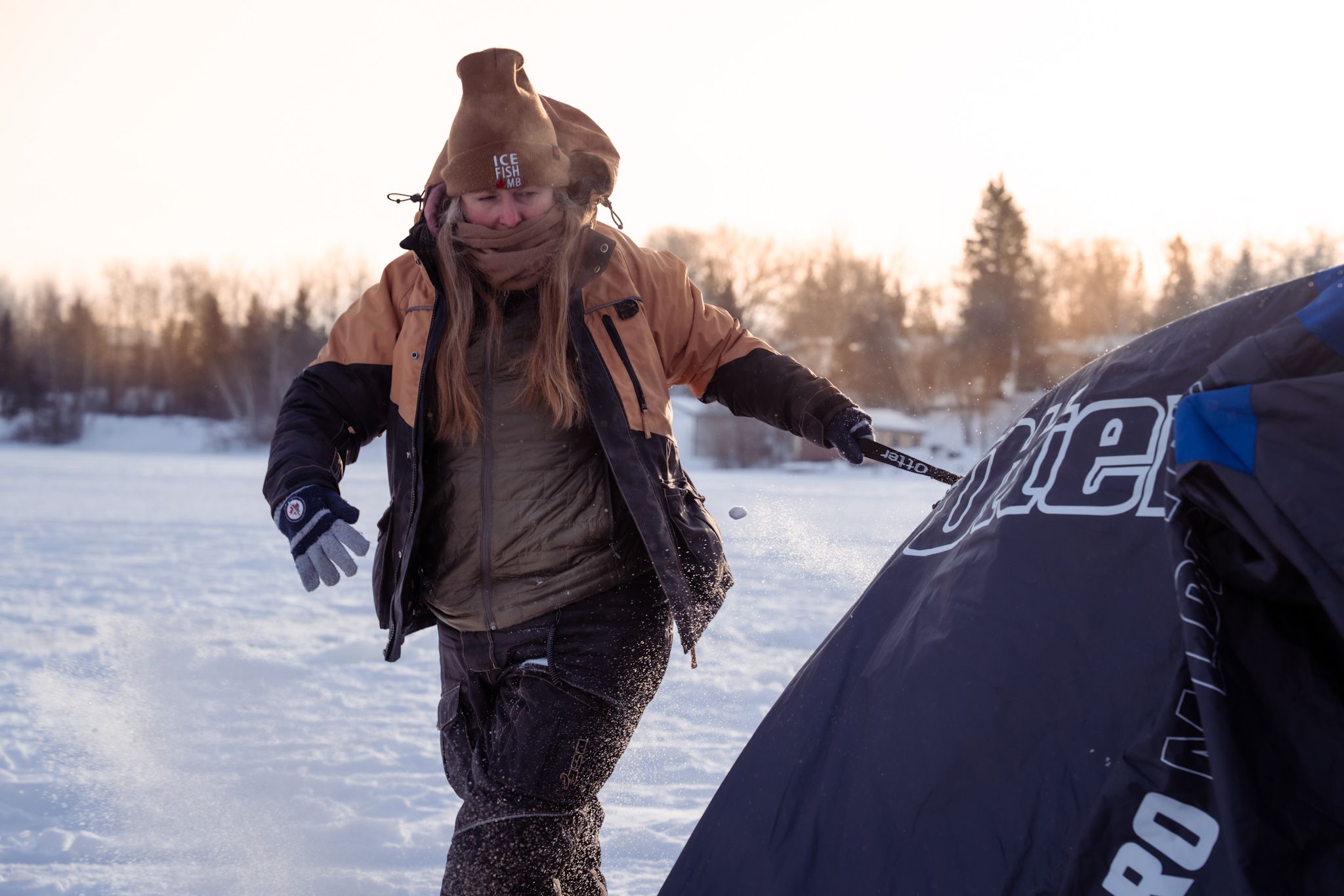 A person in winter clothing walking through a snowy landscape next to a snowmobile at sunset.